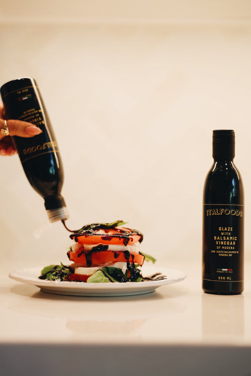 Balsamic vinegar being poured onto a salad with a bottle of Balsamic Vinegar on a white plate.